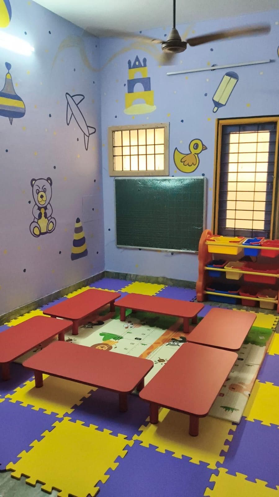 Bright classroom with activity tables, chalkboard and soft play mat